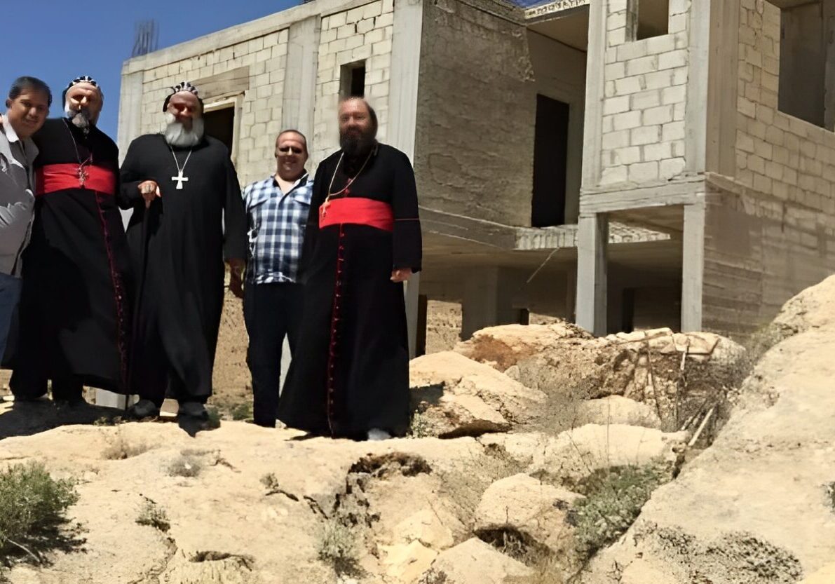Group posing by unfinished building in desert.